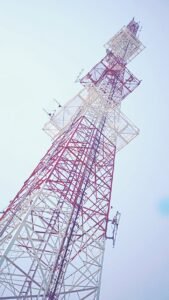 Low angle view of a red and white communication tower against a clear blue sky, capturing modern technology.